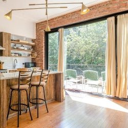 A modern kitchen with a breakfast bar, high stools, and open patio doors leading to an outdoor terrace
